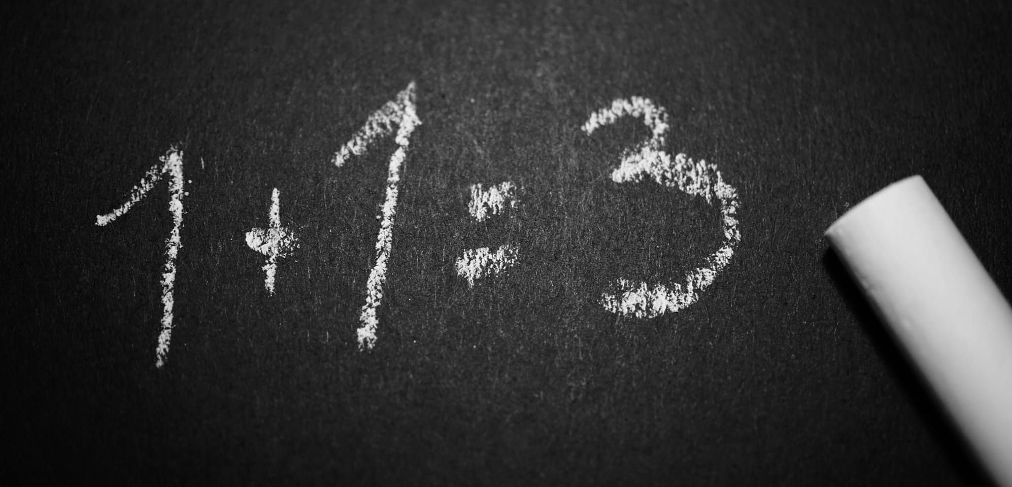 Close-up of black paper, on which is written in chalk "1+1=3."