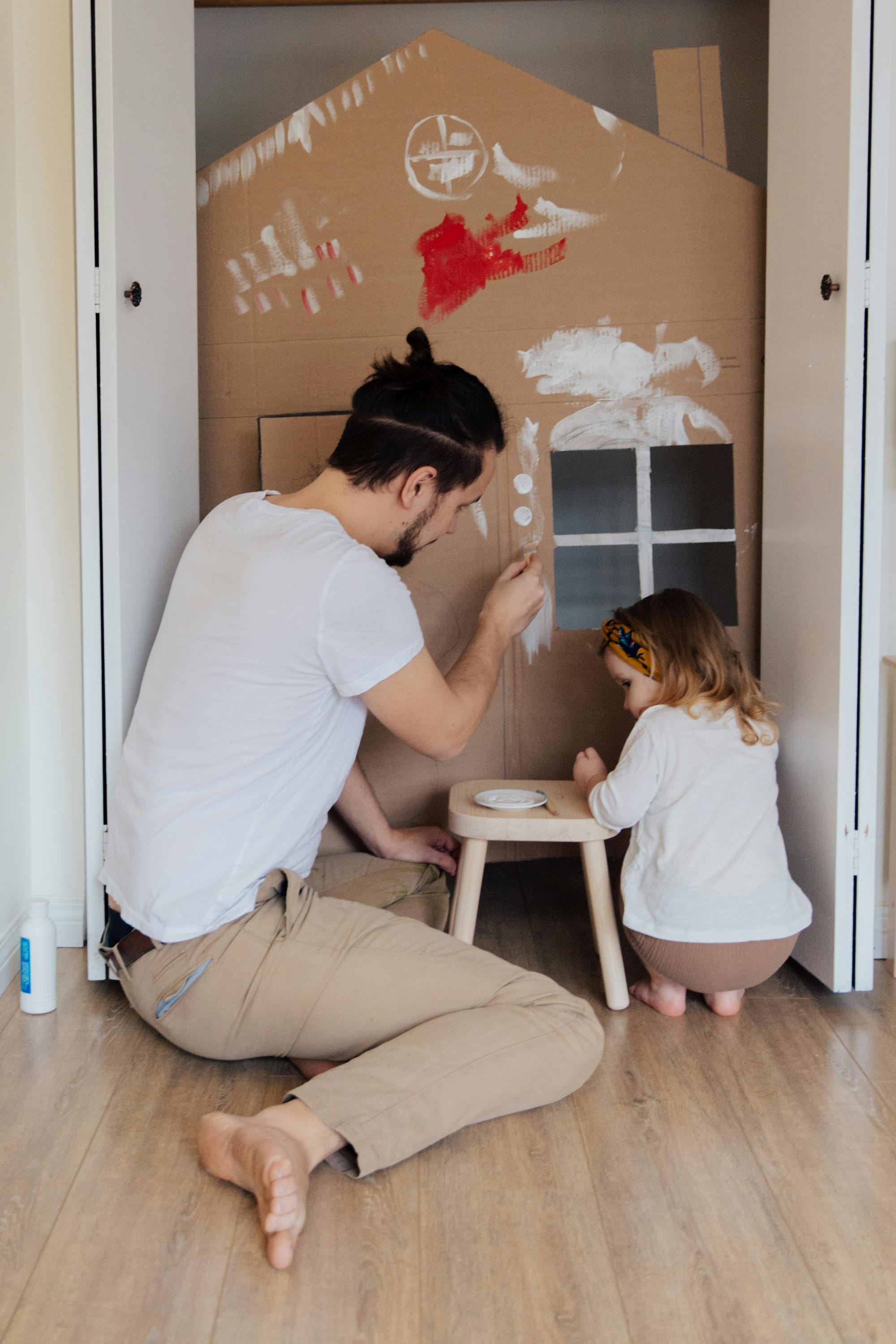 Father and daughter painting a cardboard house together.