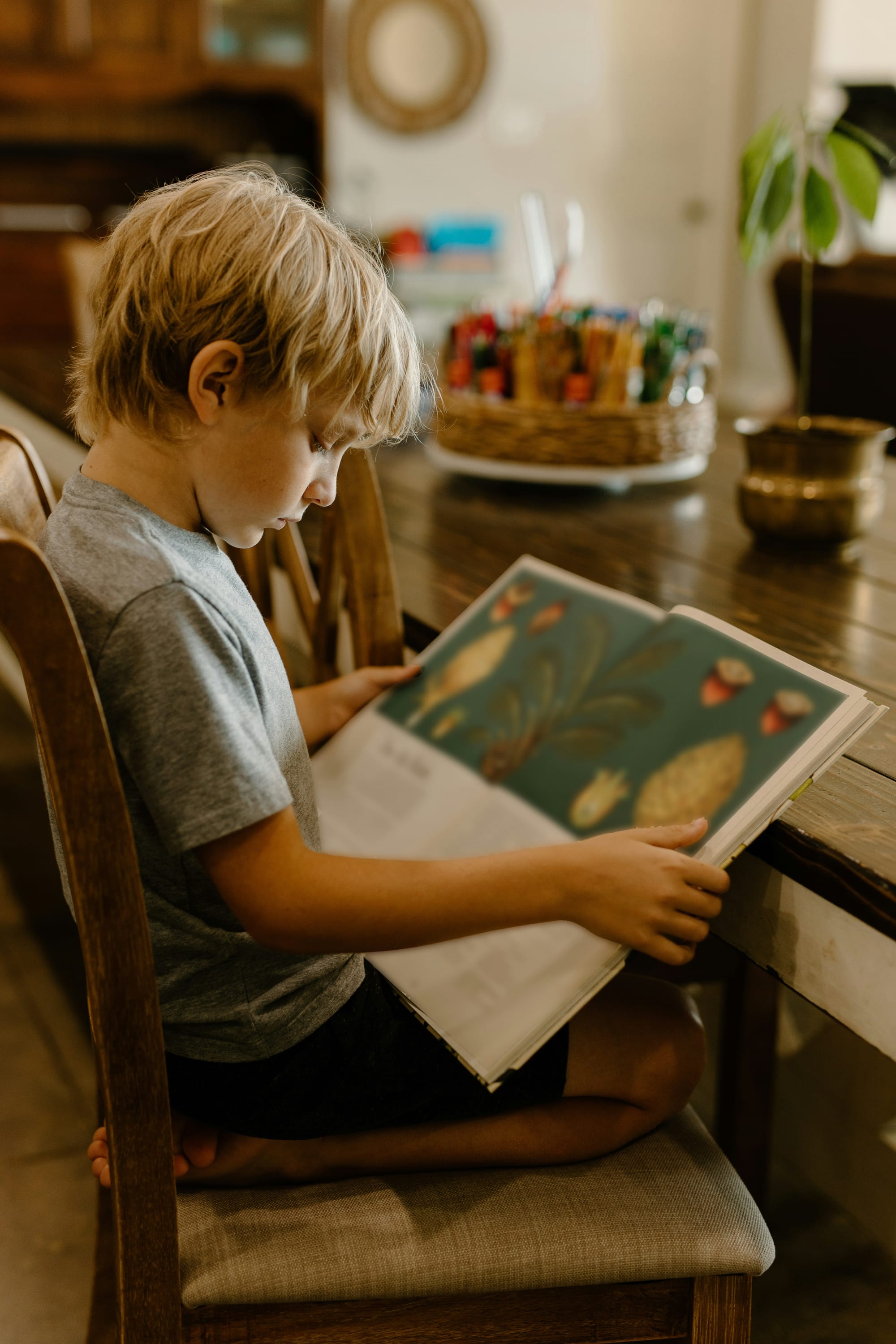 A young boy reading a picture book at a wooden table.