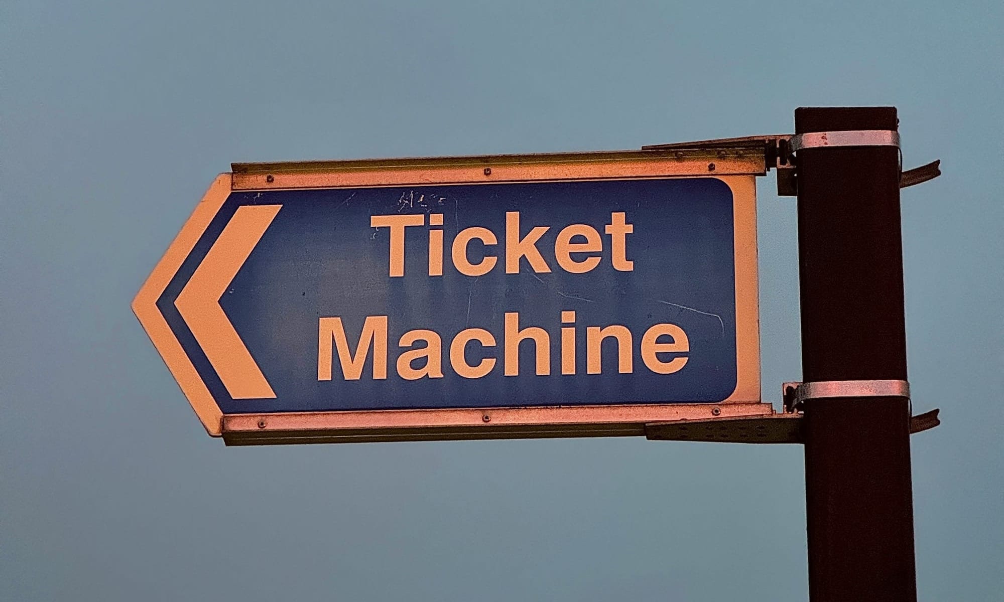 A sign on a pole pointing to the left; the words "Ticket Machine" are on the sign. 