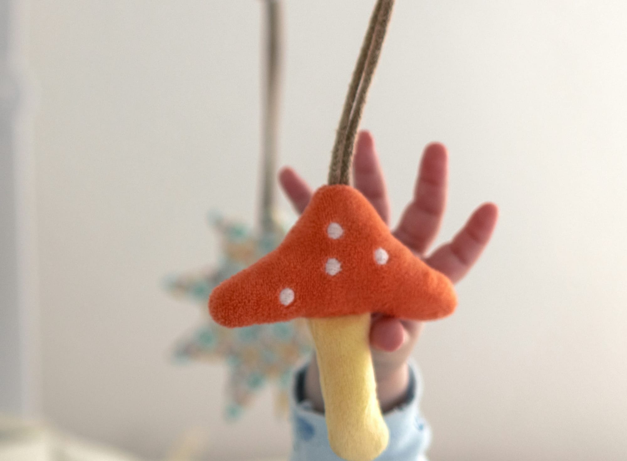 A baby's hand reaches for a felted mushroom that is part of a crib mobile.