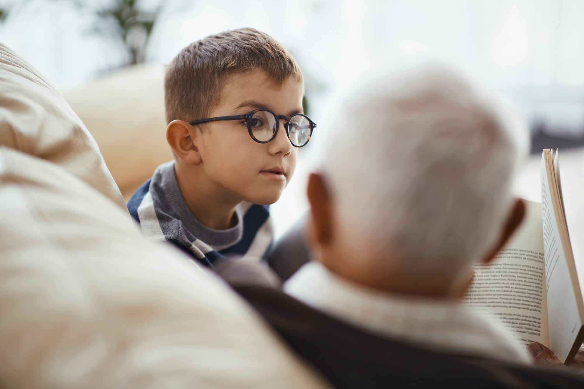 A grandchild listening attentively to his grandfather, who has a book open.