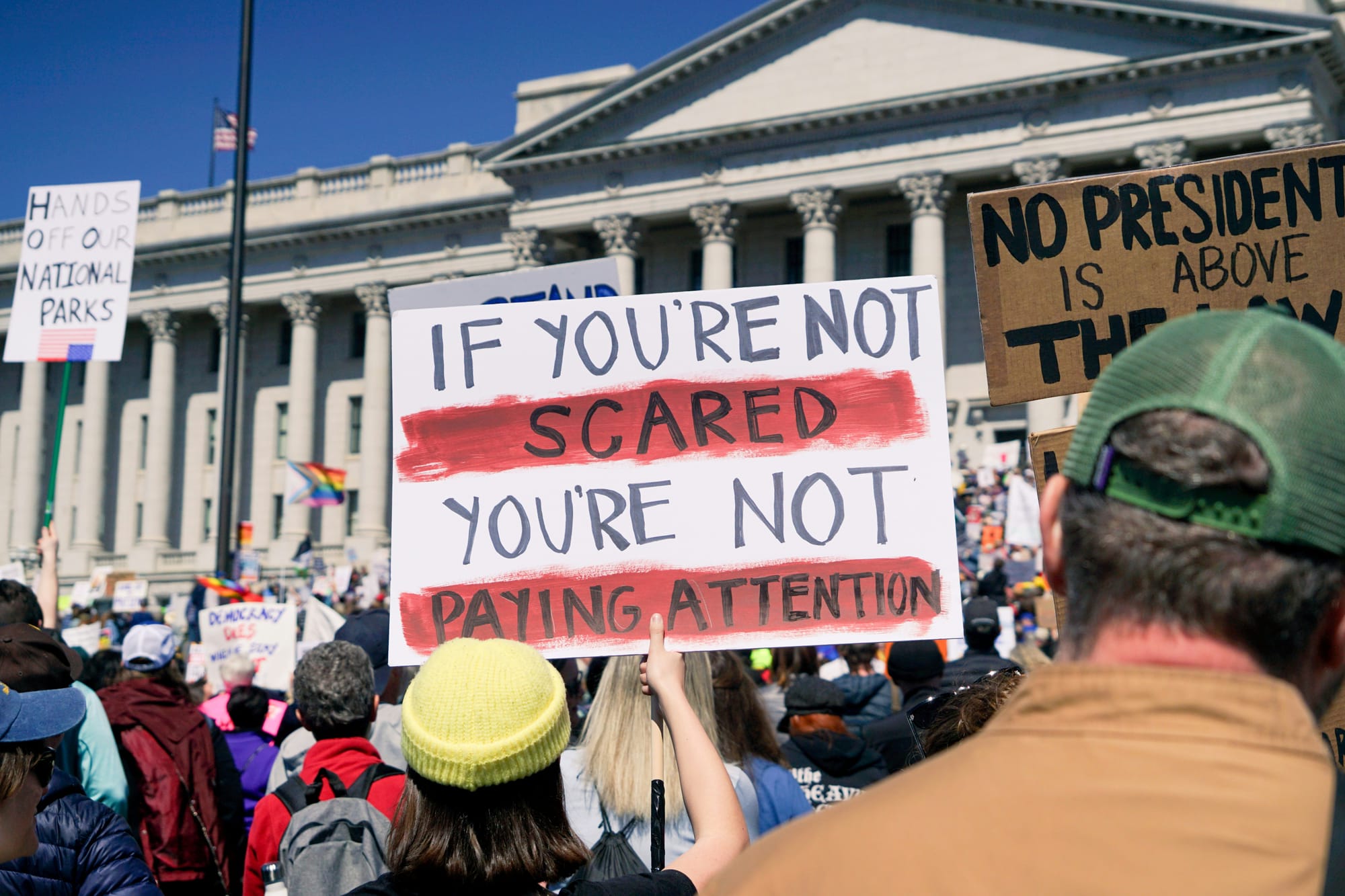 A crowd at a political rally, featuring a sign that reads, "If you're not scared, you're not paying attention."