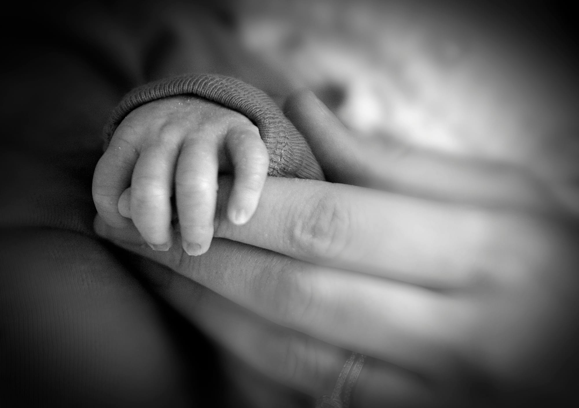 A baby's fingers wrap around an adult's index finger.