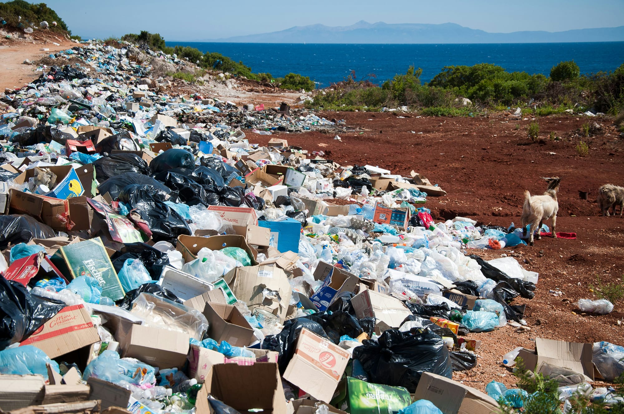 Great heaps of garbage mar the scene near a coastline.
