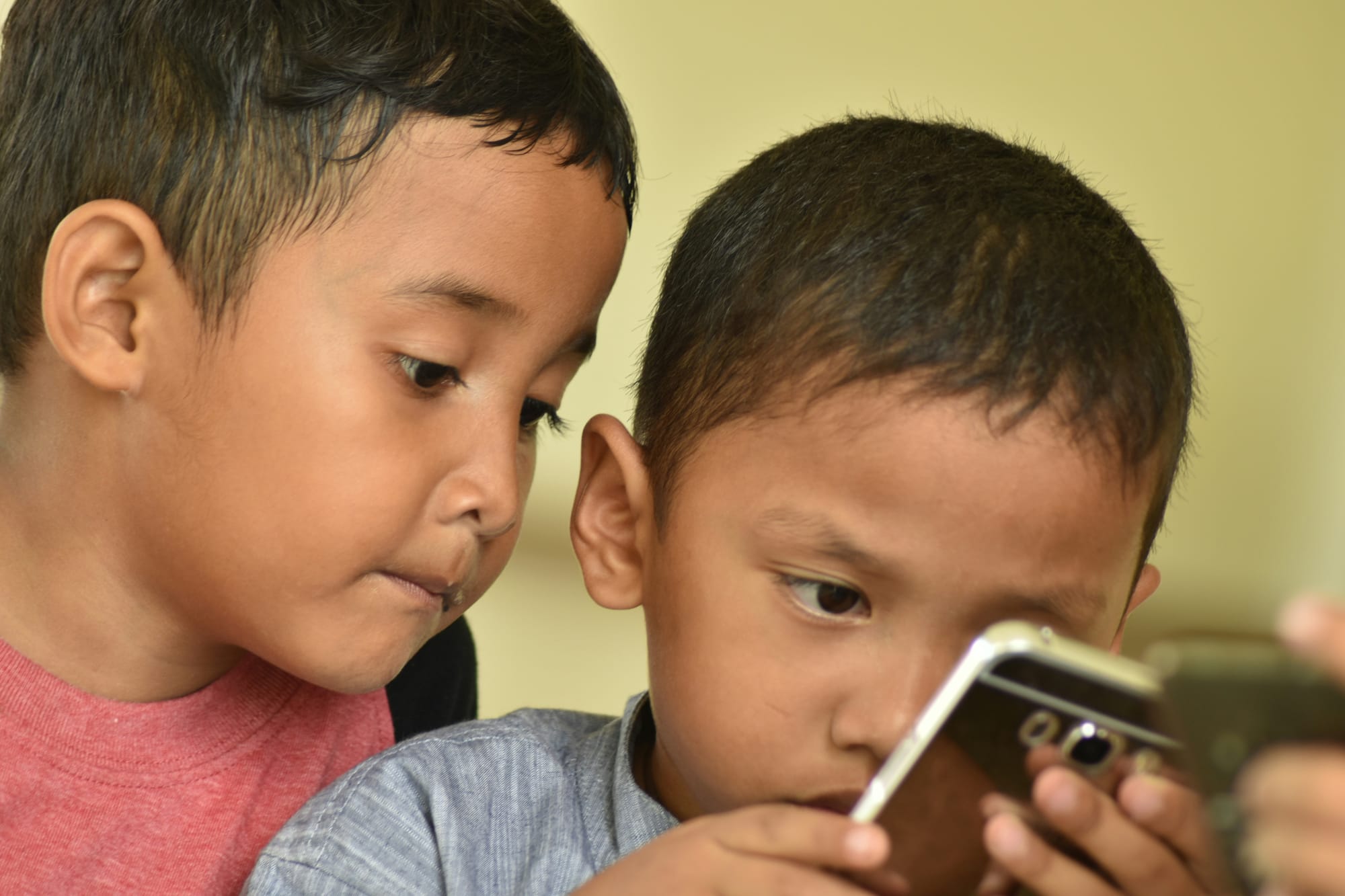 Two young boys stare intently at the smartphone one of them is holding.