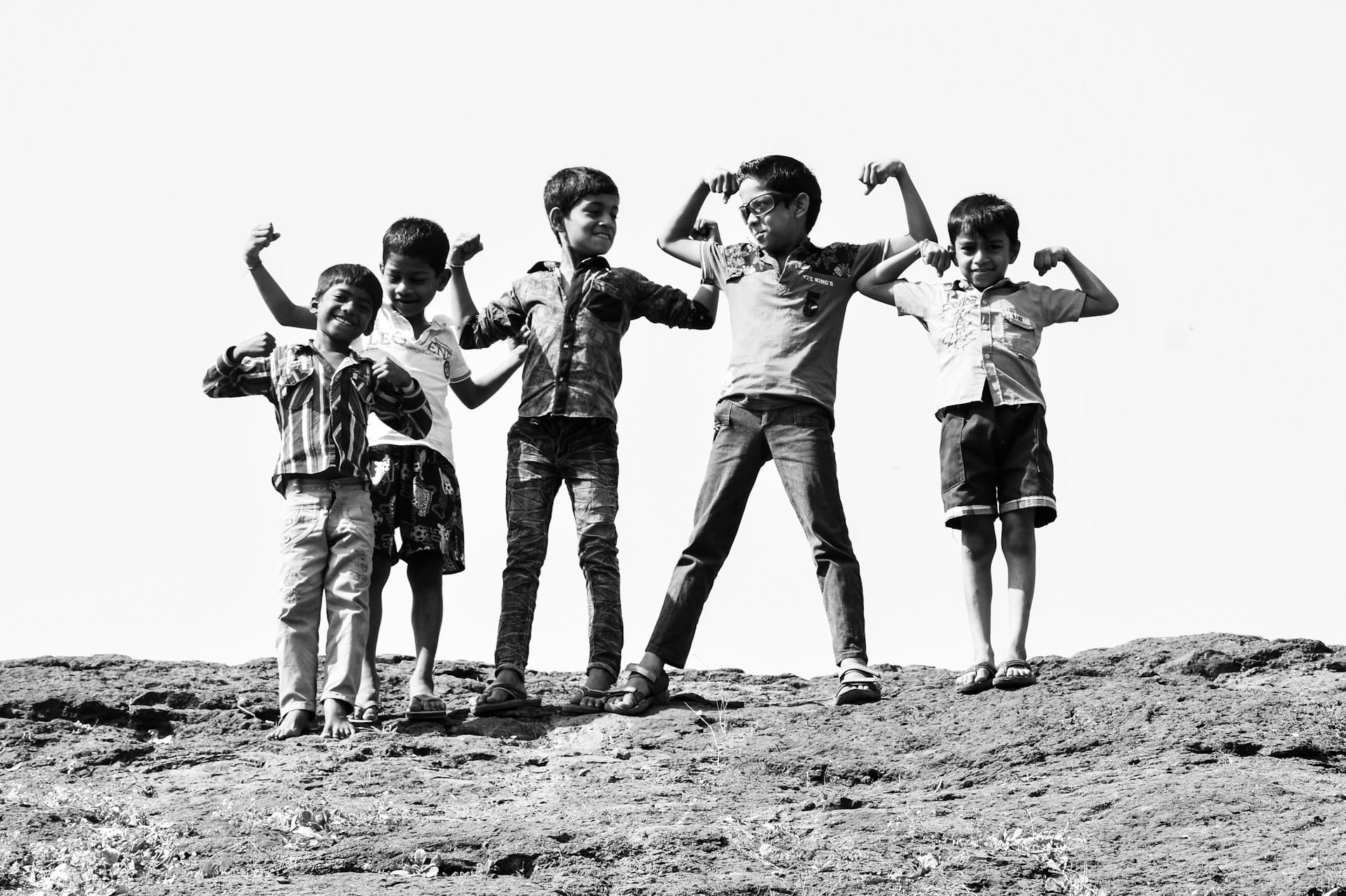 Five grade-school age boys stand on a rocky rise smiling and showing off their biceps.