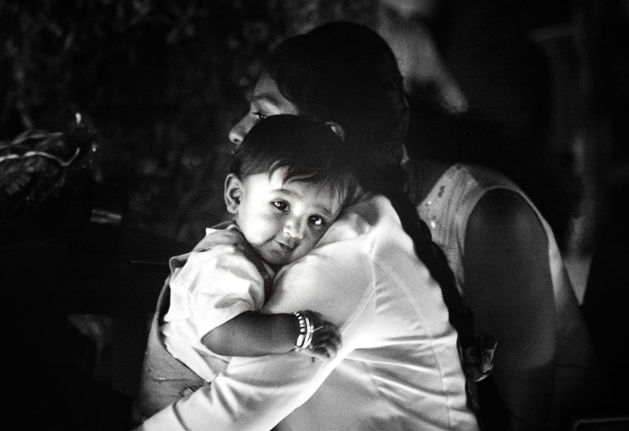 A mother holds her toddler close. The child's expression and posture suggest relaxation and contentment, although the mother appears alert to something else.