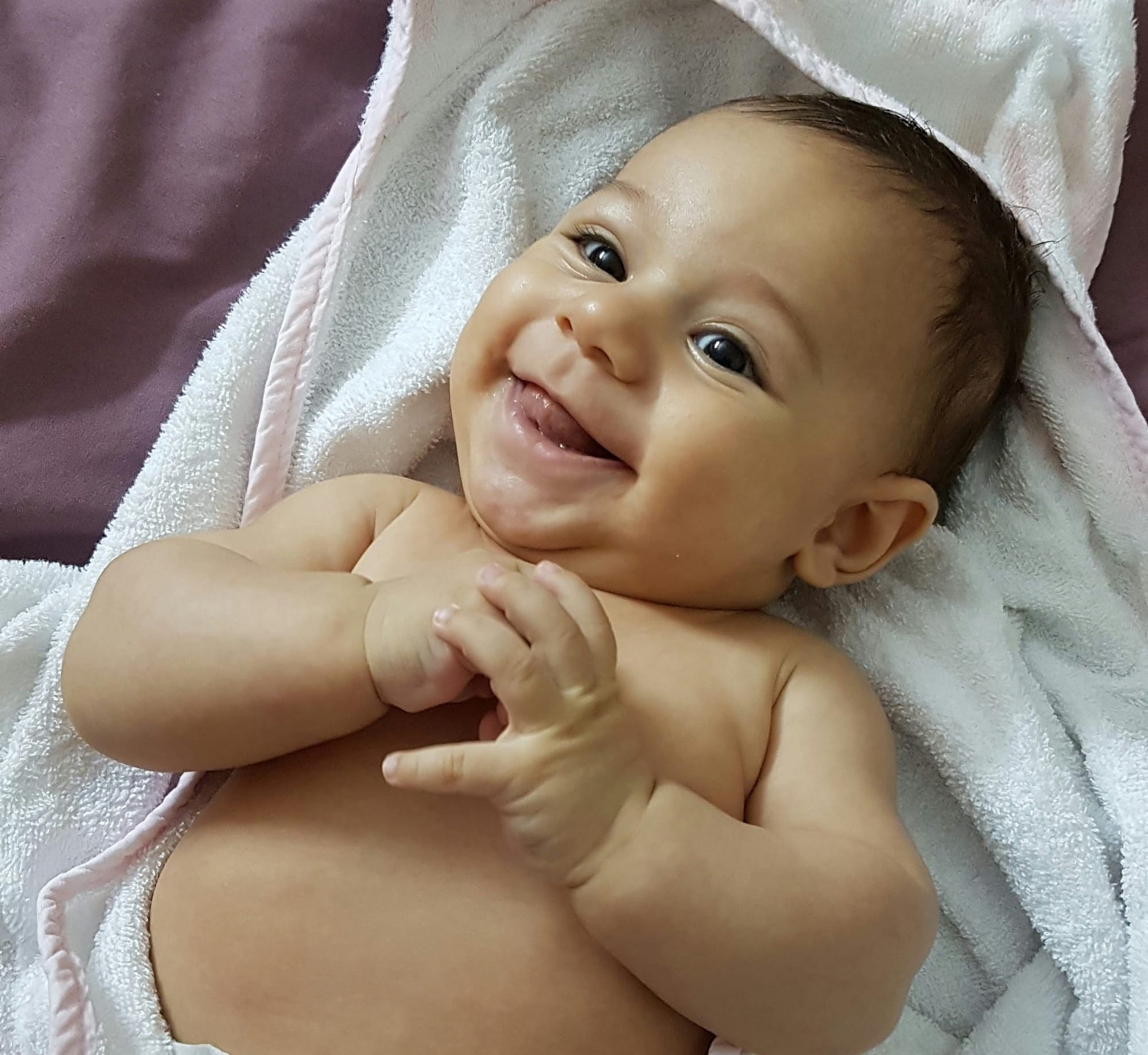 A smiling baby lies on a white bath towel. 
