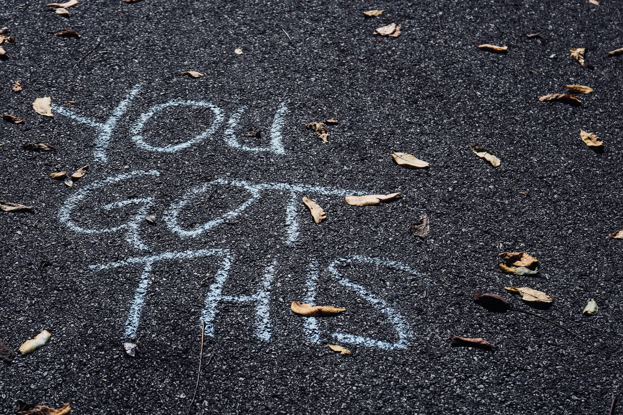 Printed on an asphalt surface in white chalk, "You got this."